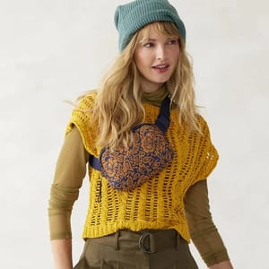 A small, patterned belt bag worn across the body, featuring a distinctive paisley design, front zipper pocket, and adjustable blue strap.