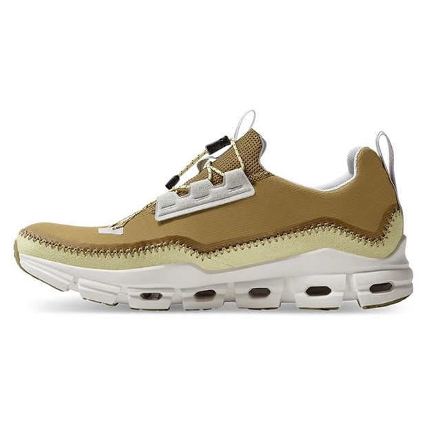 Tan and white sneaker featuring a mesh upper with unique lacing system, a distinctive wave-pattern stitch, and a cushioned, segmented sole for enhanced flexibility and comfort.