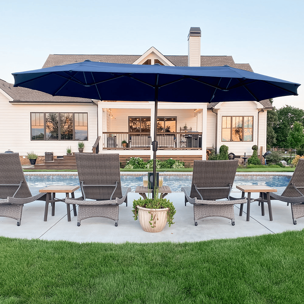 A patio scene features woven lounge chairs and a large blue patio umbrella by a pool, with a white house and green lawn in the background.
