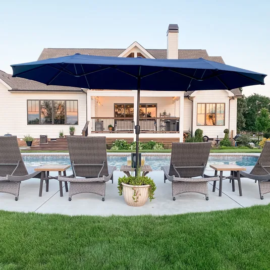 A patio scene features woven lounge chairs and a large blue patio umbrella by a pool, with a white house and green lawn in the background.