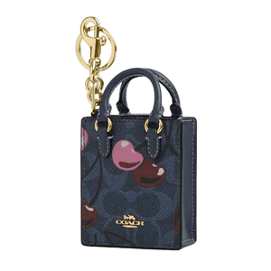 A Coach mini tote bag charm with a gold keychain, featuring a dark blue background decorated with colorful cherries and the brand's logo.