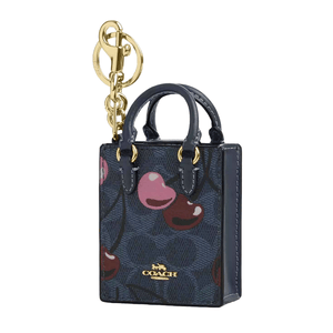 A Coach mini tote bag charm with a gold keychain, featuring a dark blue background decorated with colorful cherries and the brand's logo.