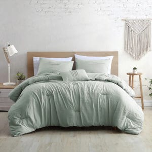 A mint green duvet cover set with pillowcases on a bed, complemented by a white bedside lamp and a woven wall hanging.