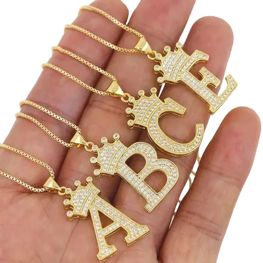 Gold necklaces with large, crown-topped letters \“A,\“ \“B,\“ and \“C\“ encrusted with small diamonds, displayed on a hand.