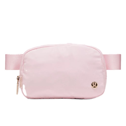 A light pink crossbody bag with a zipper and an adjustable strap, featuring a small logo emblem on the front.