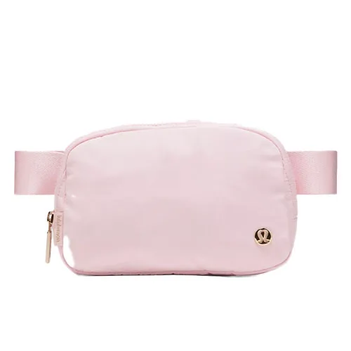 A light pink crossbody bag with a zipper and an adjustable strap, featuring a small logo emblem on the front.