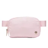 A light pink crossbody bag with a zipper and an adjustable strap, featuring a small logo emblem on the front.
