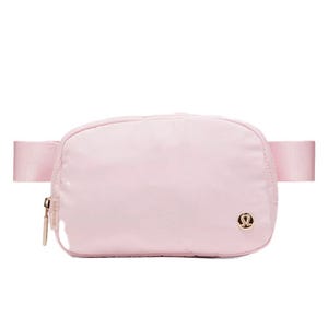 A light pink crossbody bag with a zipper and an adjustable strap, featuring a small logo emblem on the front.