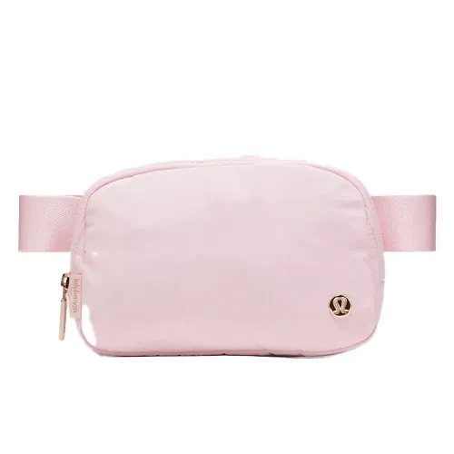 A light pink crossbody bag with a zipper and an adjustable strap, featuring a small logo emblem on the front.