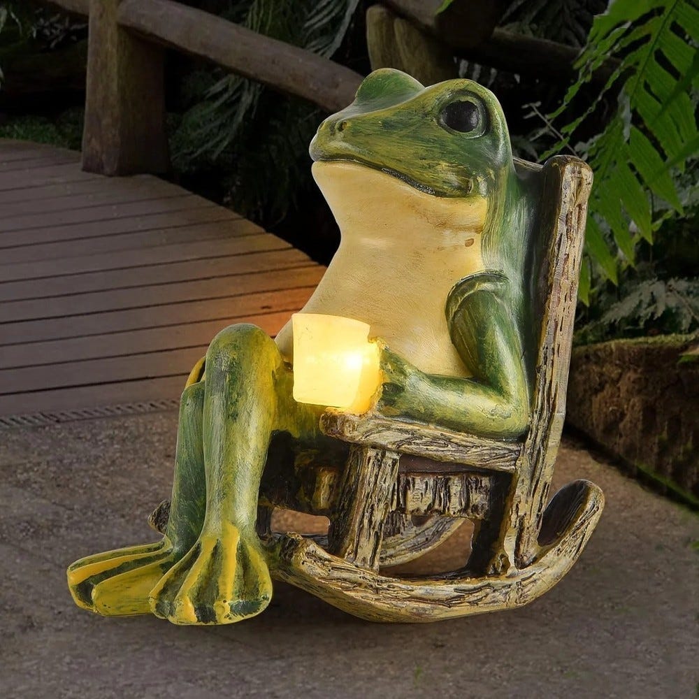 A frog figurine sits in a rustic rocking chair, holding a glowing candle. The setting suggests a garden or outdoor space.