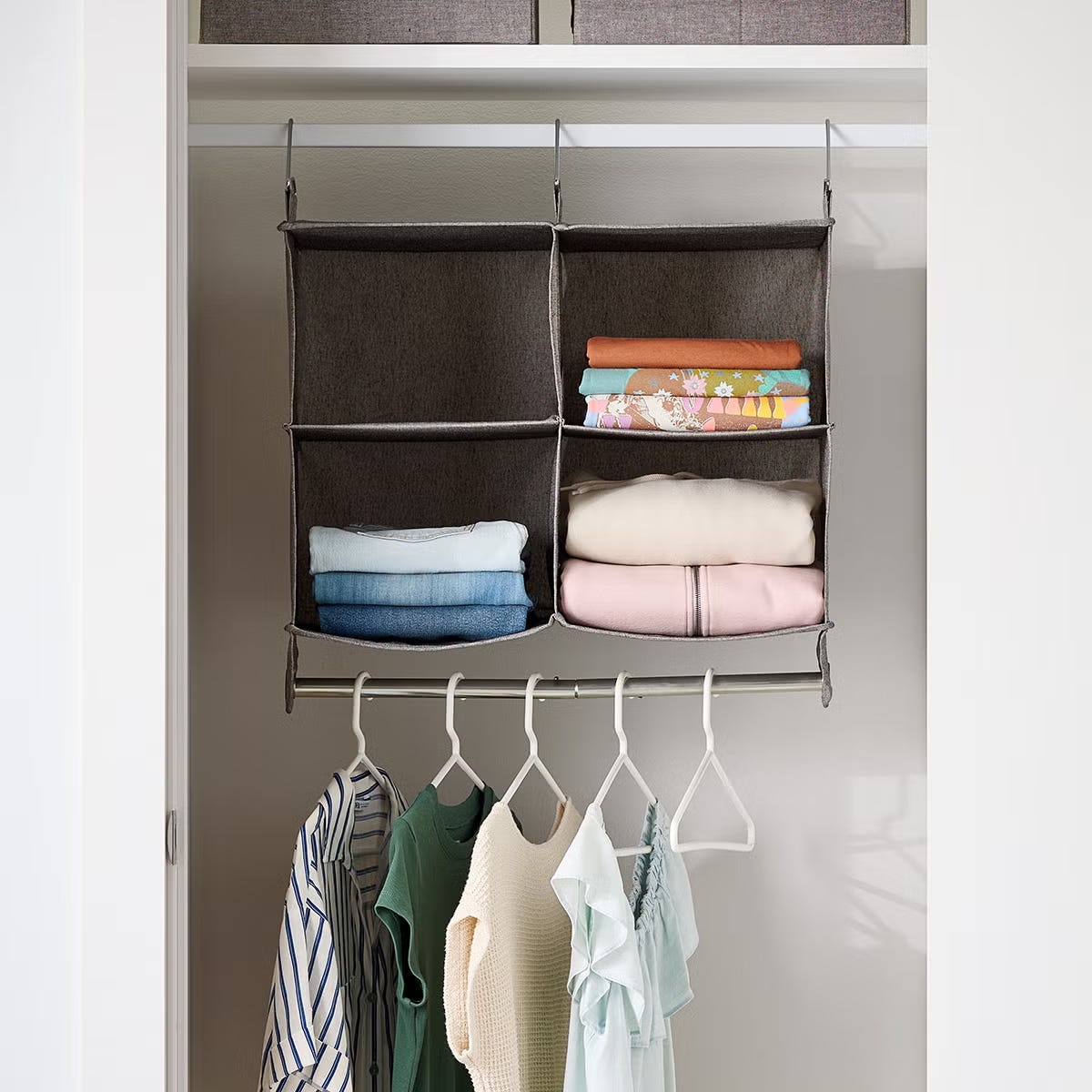 A closet with a hanging fabric organizer containing folded clothes, and a rail with hangers holding various garments.