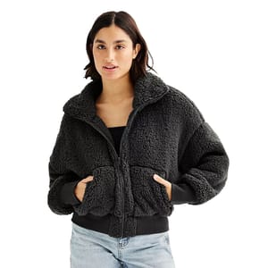 A woman is wearing a black, cozy fleece jacket with a zipper and pockets, paired with light blue jeans.