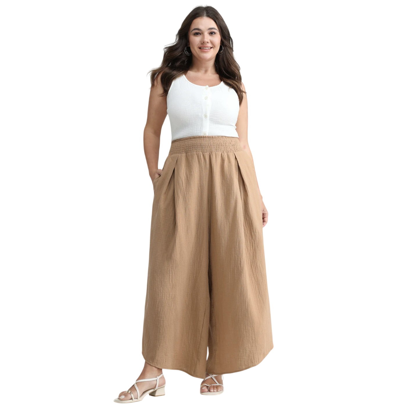 A woman is wearing a white sleeveless top with buttons and high-waisted, wide-leg tan pants, paired with white strappy sandals.