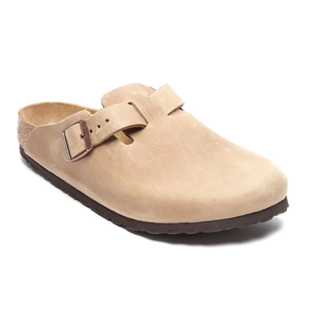 A tan-colored clog sandal with a closed toe, featuring a brown buckle strap and a cork footbed, designed for comfort and support.