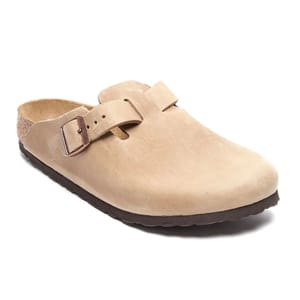 A tan-colored clog sandal with a closed toe, featuring a brown buckle strap and a cork footbed, designed for comfort and support.