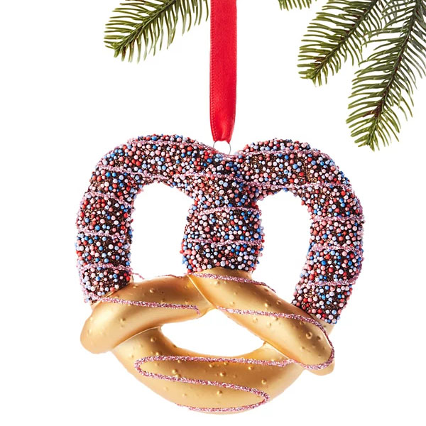 A pretzel-shaped Christmas ornament decorated with colorful nonpareils hanging from a red ribbon.