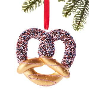A pretzel-shaped Christmas ornament decorated with colorful nonpareils hanging from a red ribbon.