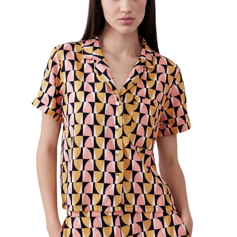 A short-sleeve pajama set features a bold geometric pattern in pink, yellow, and black with a button-up top and matching shorts.