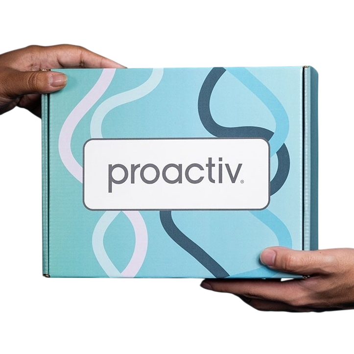 A Proactiv package is being held by two hands against a blue background. The box features a simple design with wavy lines and the brand's name prominently displayed.