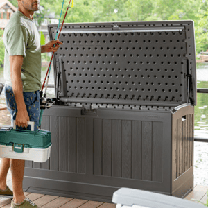 A dark gray Suncast deck box bench with a 200-gallon capacity, featuring a hinged lid with a pegboard pattern on the interior. It serves as storage, shown open with a person holding fishing gear nearby.