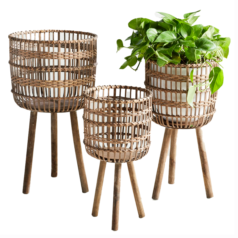 Set of 3 planters made of woven bamboo and wood, each featuring a tripod stand. Two have empty baskets, and the third holds a leafy green plant. The design is rustic and stylish.