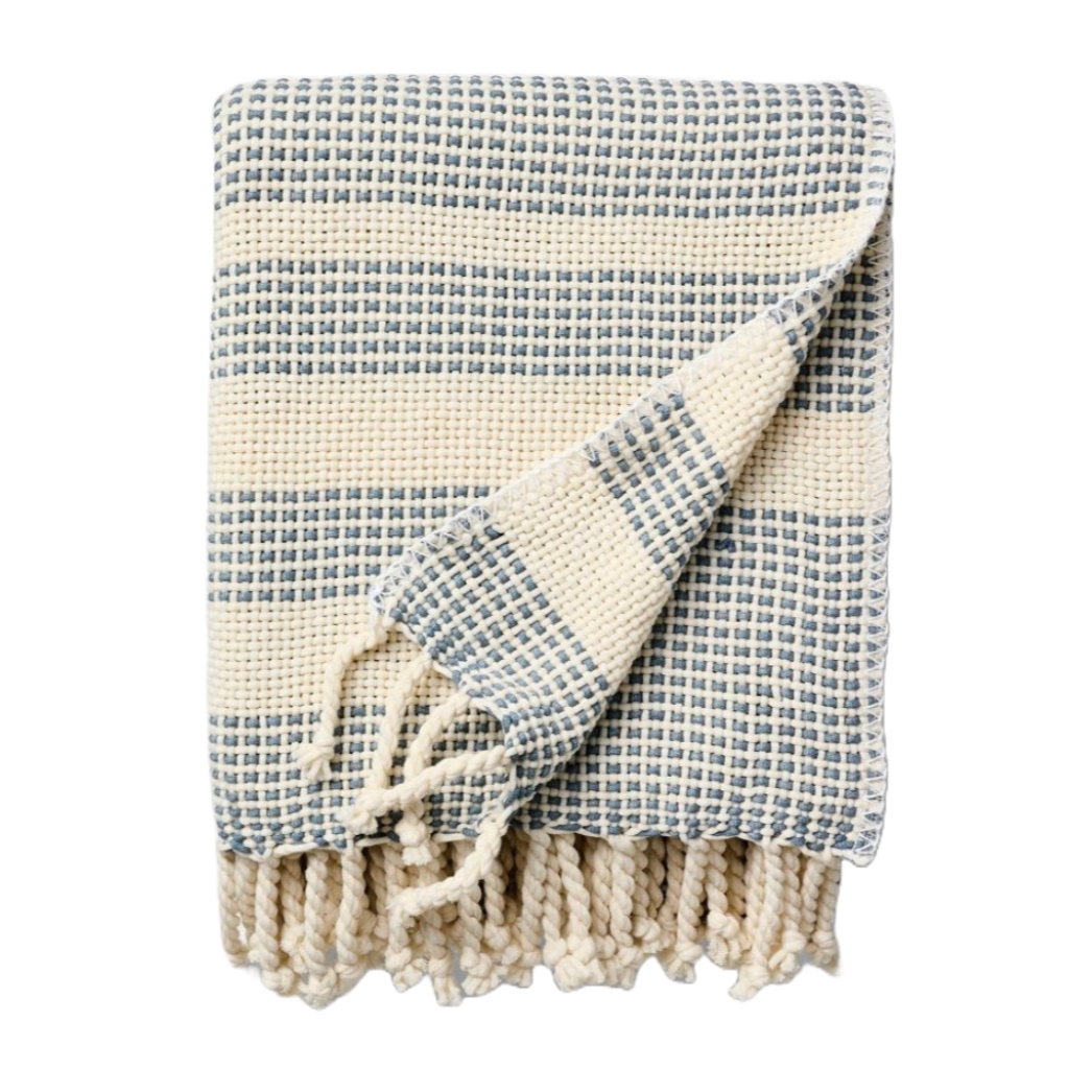 A woven throw featuring a pattern of blue and cream stripes with a textured weave and tasseled edges.