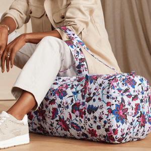A person seated holding a floral patterned duffel bag.
