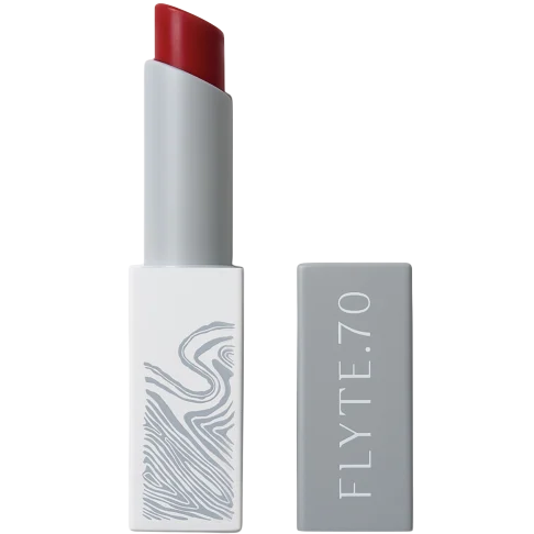 A tube of FLYTE.70 lipstick in a gray rectangular case with a red shade and abstract line design on one side.