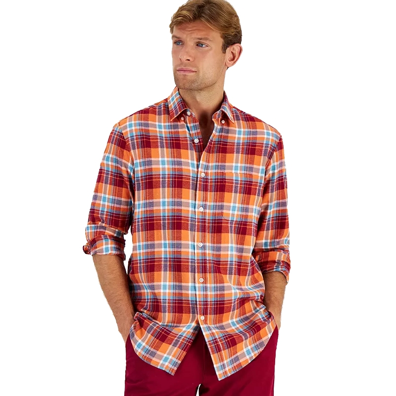 A man wears a Club Room regular-fit plaid flannel shirt, featuring a combination of red, orange, and blue checks. The shirt has a button-down front and long sleeves with the cuffs rolled up.