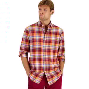 A man wears a Club Room regular-fit plaid flannel shirt, featuring a combination of red, orange, and blue checks. The shirt has a button-down front and long sleeves with the cuffs rolled up.