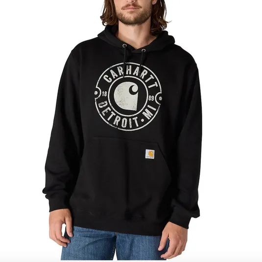 A person is wearing a black Carhartt hoodie with a \“Carhartt Detroit, MI\“ graphic, paired with blue jeans.