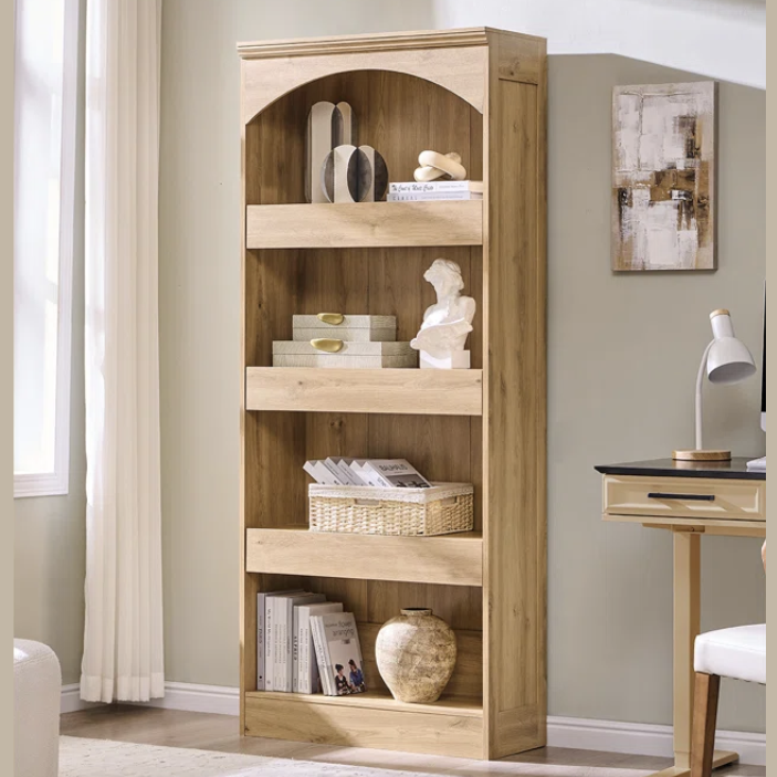 Tall wooden bookcase with multiple shelves holding decorative items like sculptures, books, and storage bins, situated next to a desk and lamp.