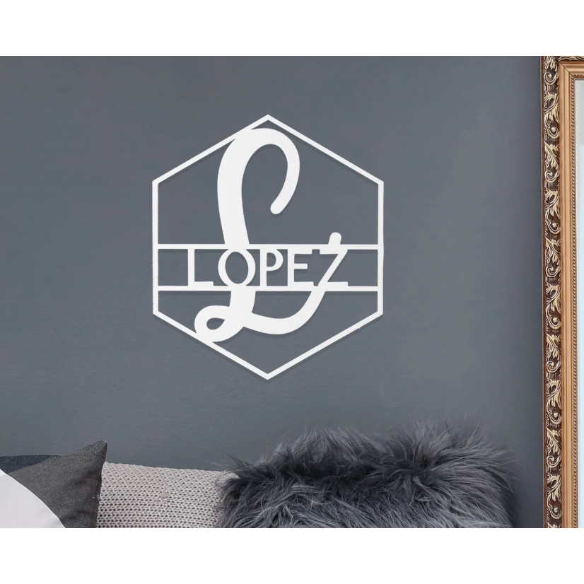 White hexagonal wall art with the name \“Lopez\“ and a large stylized letter \“L\“ on a gray wall, next to a decorative frame and fuzzy pillow.