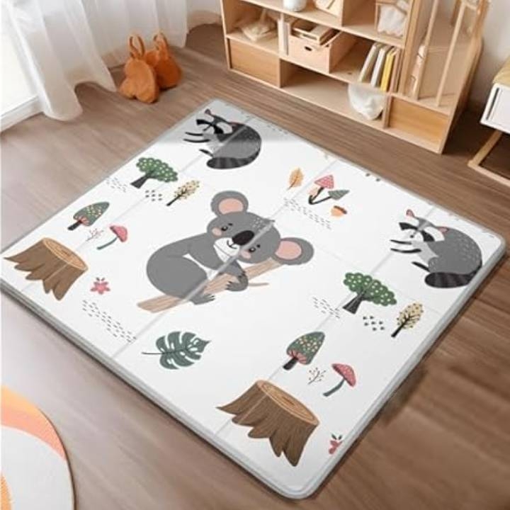 Illustrated playmat featuring a koala and raccoon among trees and mushrooms, set in a cozy room with wooden flooring and shelving unit.