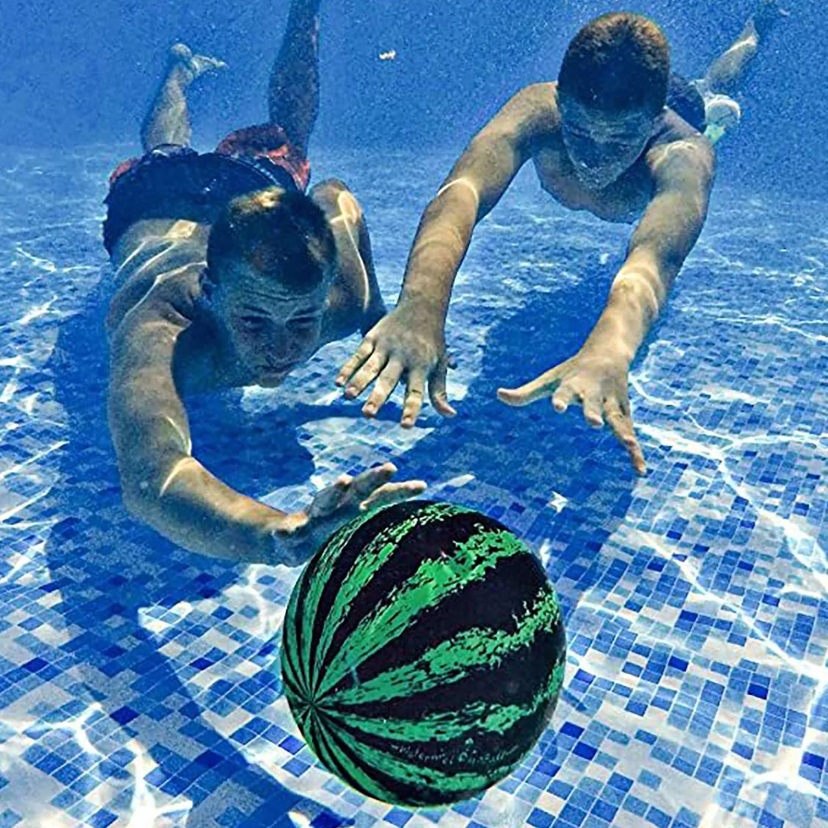 Two people are swimming underwater in a pool, reaching for a watermelon-patterned ball.