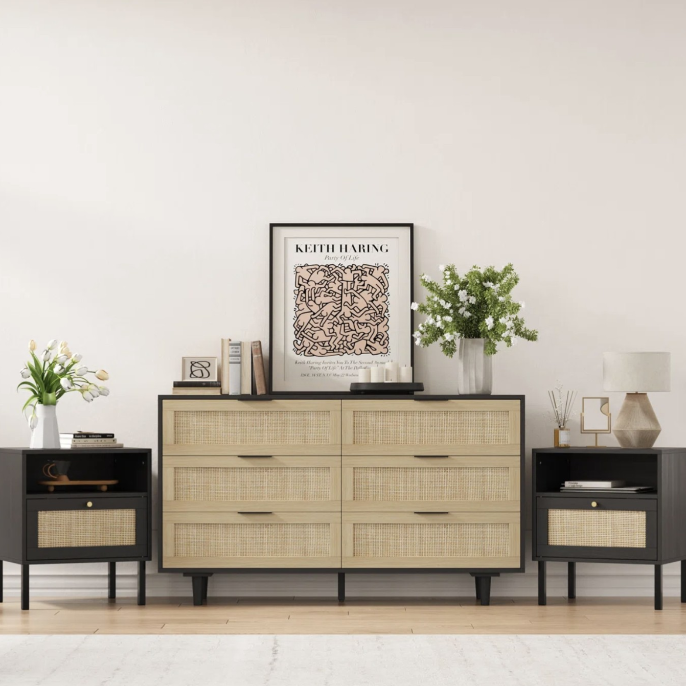 Mid-century style setup with a large dresser and two matching side tables featuring woven rattan drawer fronts and black accents. Decor includes a Keith Haring artwork, books, candles, a lamp, and vases with flowers.