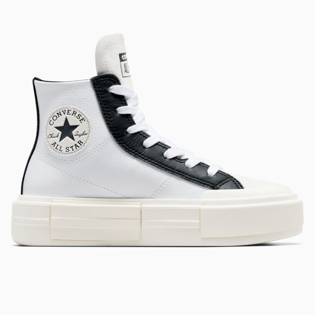 White high-top canvas sneaker with a black classic logo patch, thick platform sole, and black-and-white laces.