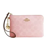 A pink Coach wristlet with gold hardware and a floral charm, featuring a subtle embossed pattern and detachable leather strap.