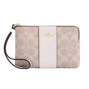 A beige Coach wristlet with a signature pattern, featuring a white vertical stripe and gold logo detailing.