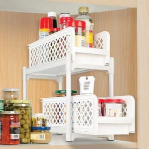 A two-pack of white, two-tiered sliding cabinet organizers with a lattice design, used for storing and organizing kitchen items on shelves.