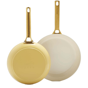 Two GreenPan nonstick frying pans with ceramic coatings and gold-toned handles are shown. One pan is positioned bottom-up to display its exterior, while the other displays a cream-colored cooking surface.