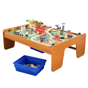 A wooden train table with a detailed railway layout, including bridges, buildings, vehicles, and figures, complete with a blue bin for additional storage.