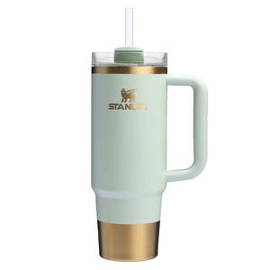 A Stanley-branded insulated tumbler with a handle, straw, and two-tone design featuring white and gold colors.