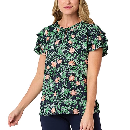 A woman is wearing a navy blue blouse with a floral pattern featuring green leaves and pink flowers, paired with dark pants. The blouse has short ruffled sleeves.
