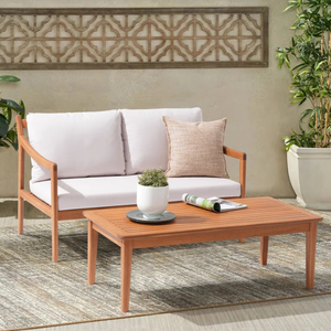 Outdoor wooden patio furniture set featuring a cushioned sofa and a coffee table, complemented by a decorative wall panel and potted plants on a textured rug.