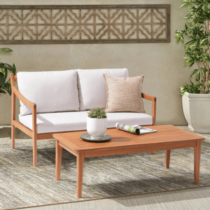Outdoor wooden patio furniture set featuring a cushioned sofa and a coffee table, complemented by a decorative wall panel and potted plants on a textured rug.