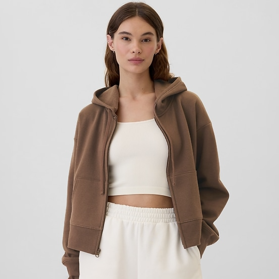 A brown fleece hooded jacket with a zippered front and drop shoulders, paired with a white cropped tank top and light-colored pants.