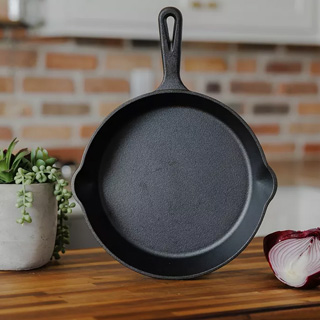 A cast iron skillet on a wooden surface, next to a plant and half an onion.
