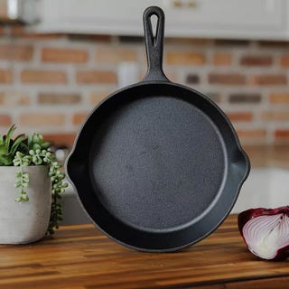 A cast iron skillet on a wooden surface, next to a plant and half an onion.