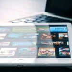 A tablet is displayed on a laptop keyboard, showing a colorful screen with various multimedia icons.